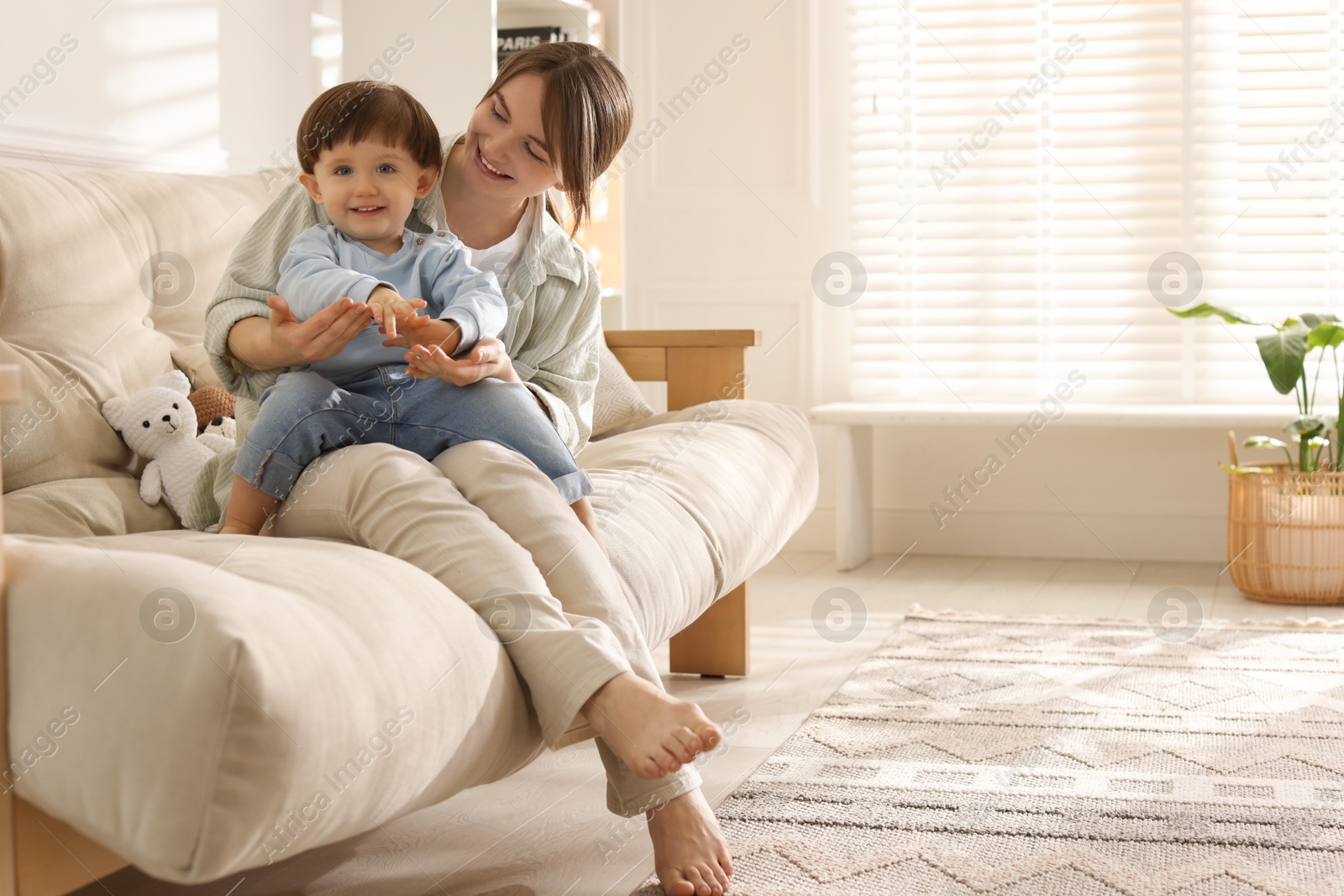 Photo of Happy mother with her cute little son on sofa at home, space for text