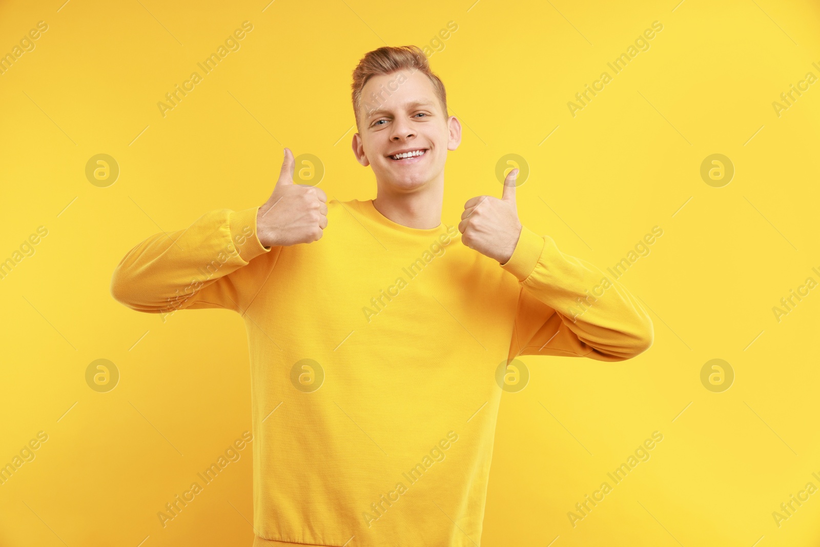 Photo of Happy man showing thumbs up on yellow background. Like gesture