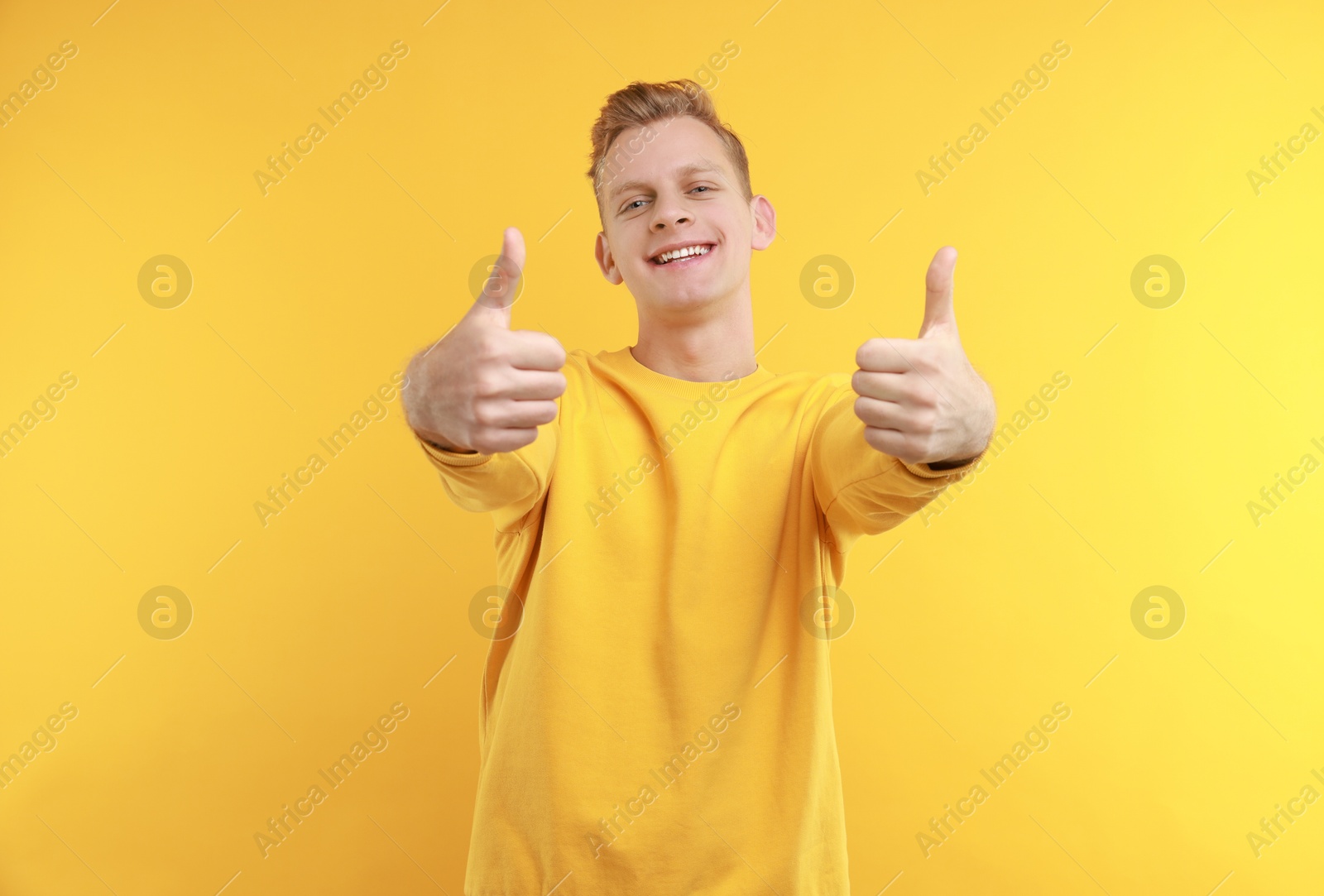 Photo of Happy man showing thumbs up on yellow background. Like gesture