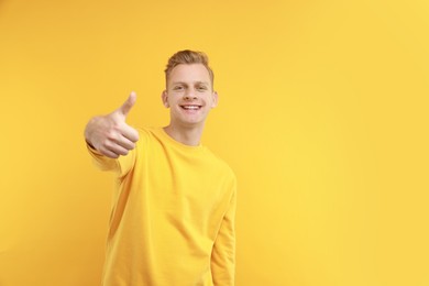 Happy man showing thumbs up on yellow background, space for text. Like gesture