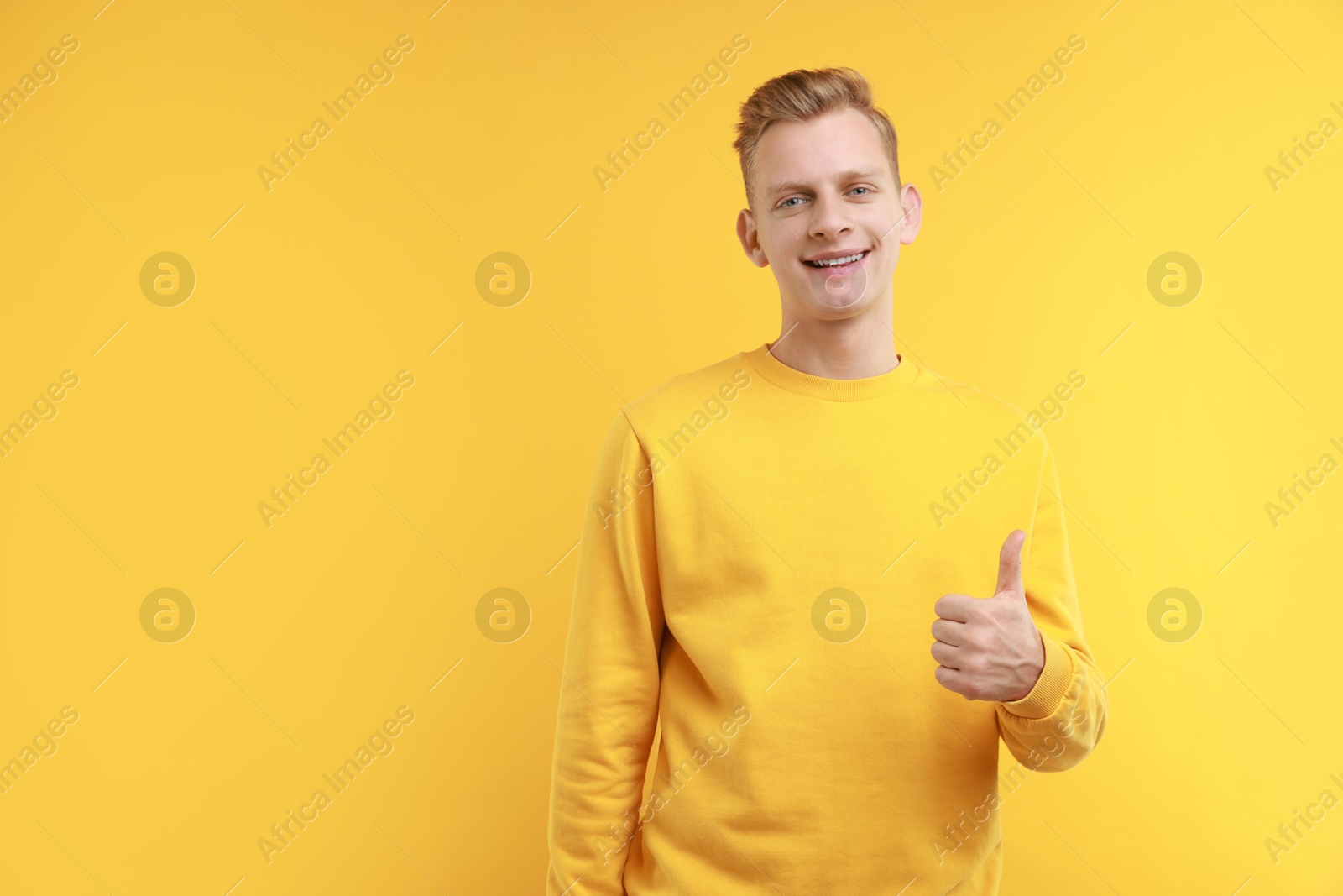 Photo of Happy man showing thumbs up on yellow background, space for text. Like gesture