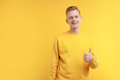 Photo of Happy man showing thumbs up on yellow background, space for text. Like gesture