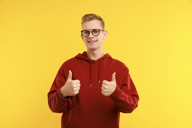 Photo of Happy man showing thumbs up on yellow background. Like gesture