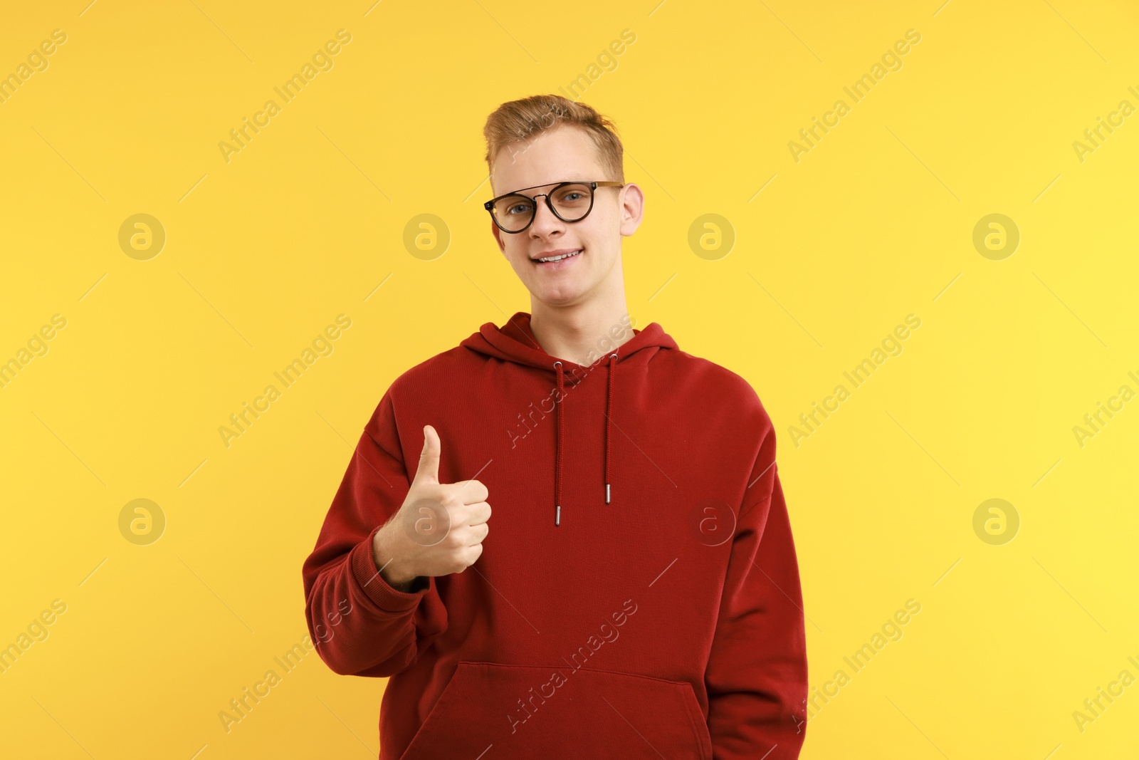 Photo of Happy man showing thumbs up on yellow background. Like gesture