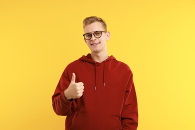 Photo of Happy man showing thumbs up on yellow background. Like gesture