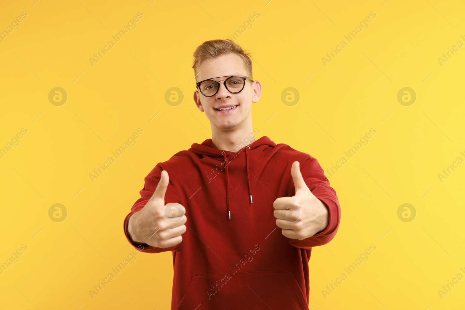 Photo of Happy man showing thumbs up on yellow background. Like gesture