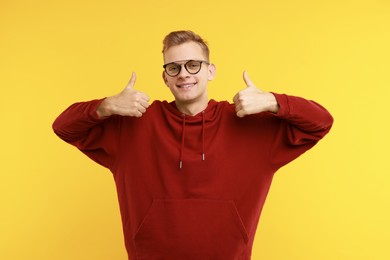 Photo of Happy man showing thumbs up on yellow background. Like gesture