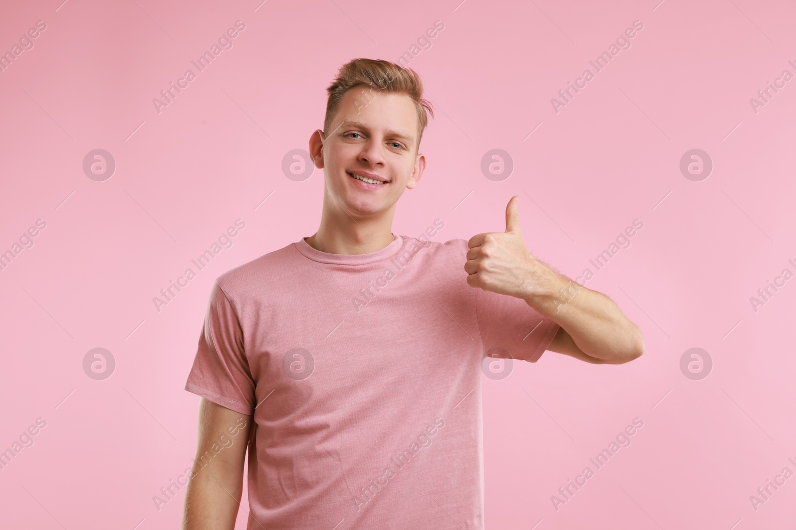 Photo of Happy man showing thumbs up on pink background. Like gesture