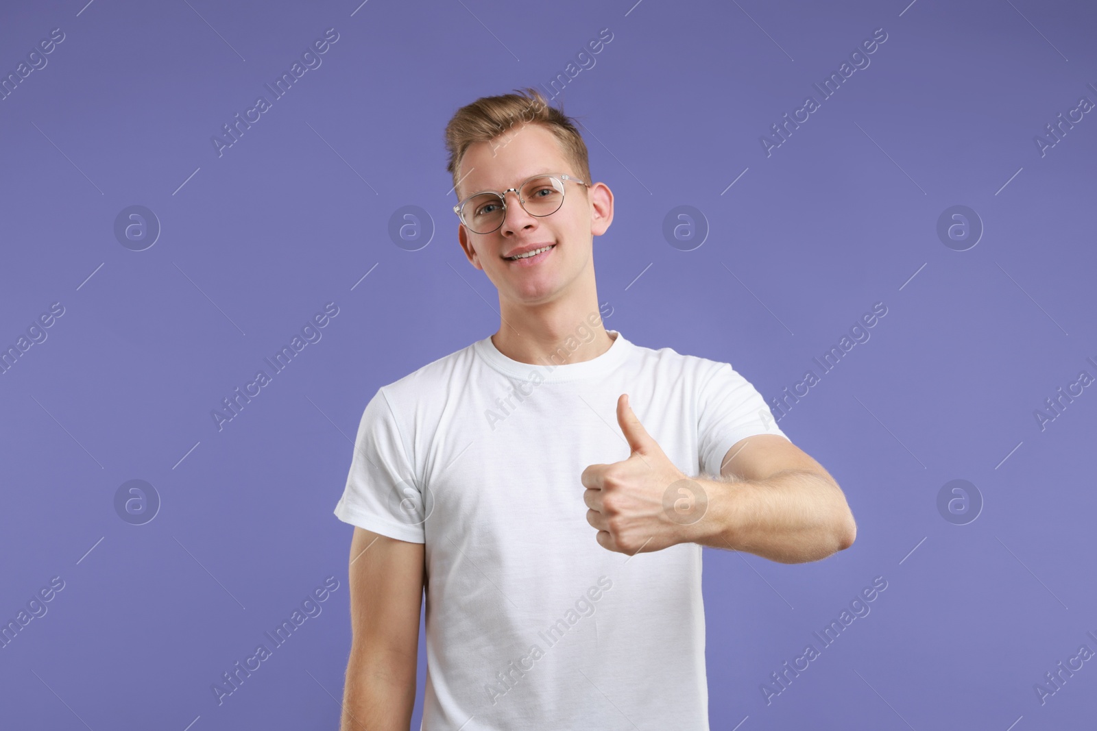 Photo of Happy man showing thumbs up on purple background. Like gesture