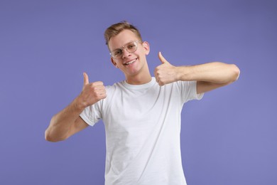 Photo of Happy man showing thumbs up on purple background. Like gesture