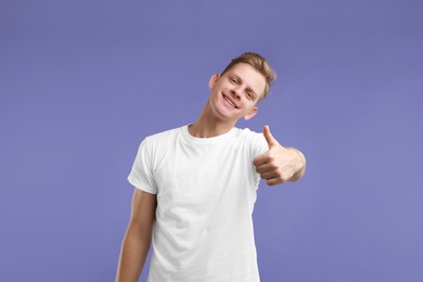 Photo of Happy man showing thumbs up on purple background. Like gesture