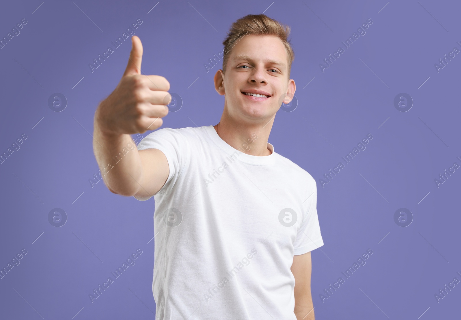 Photo of Happy man showing thumbs up on purple background. Like gesture