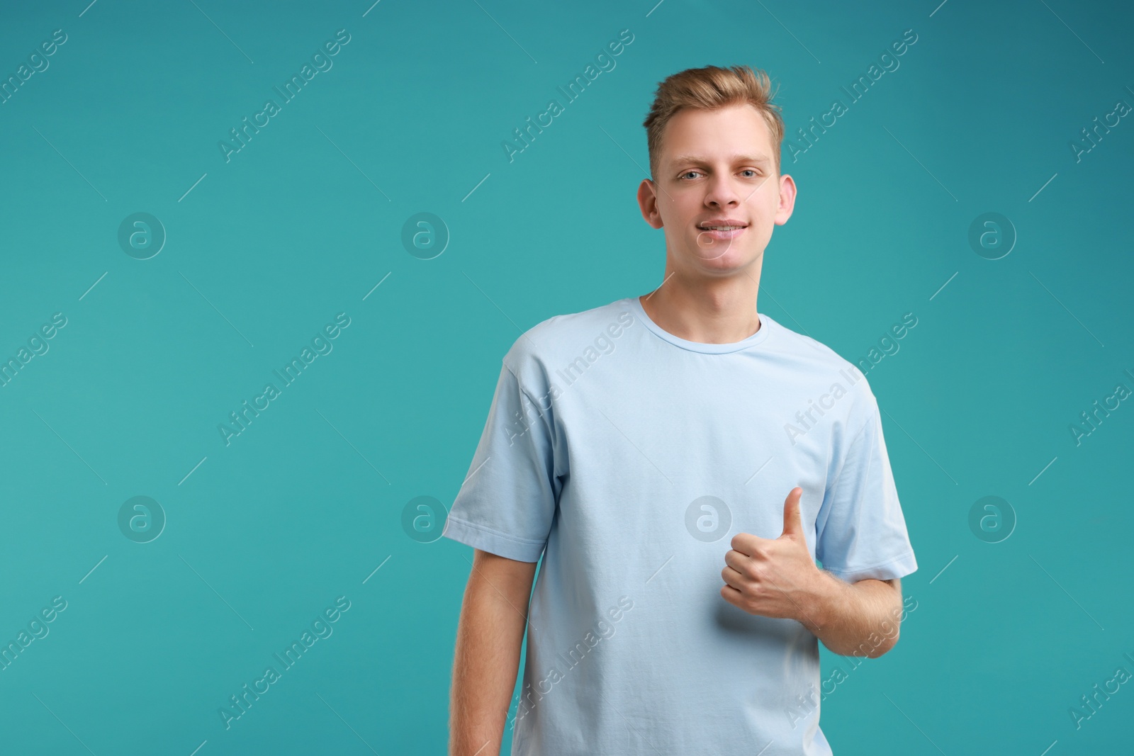 Photo of Happy man showing thumbs up on light blue background, space for text. Like gesture