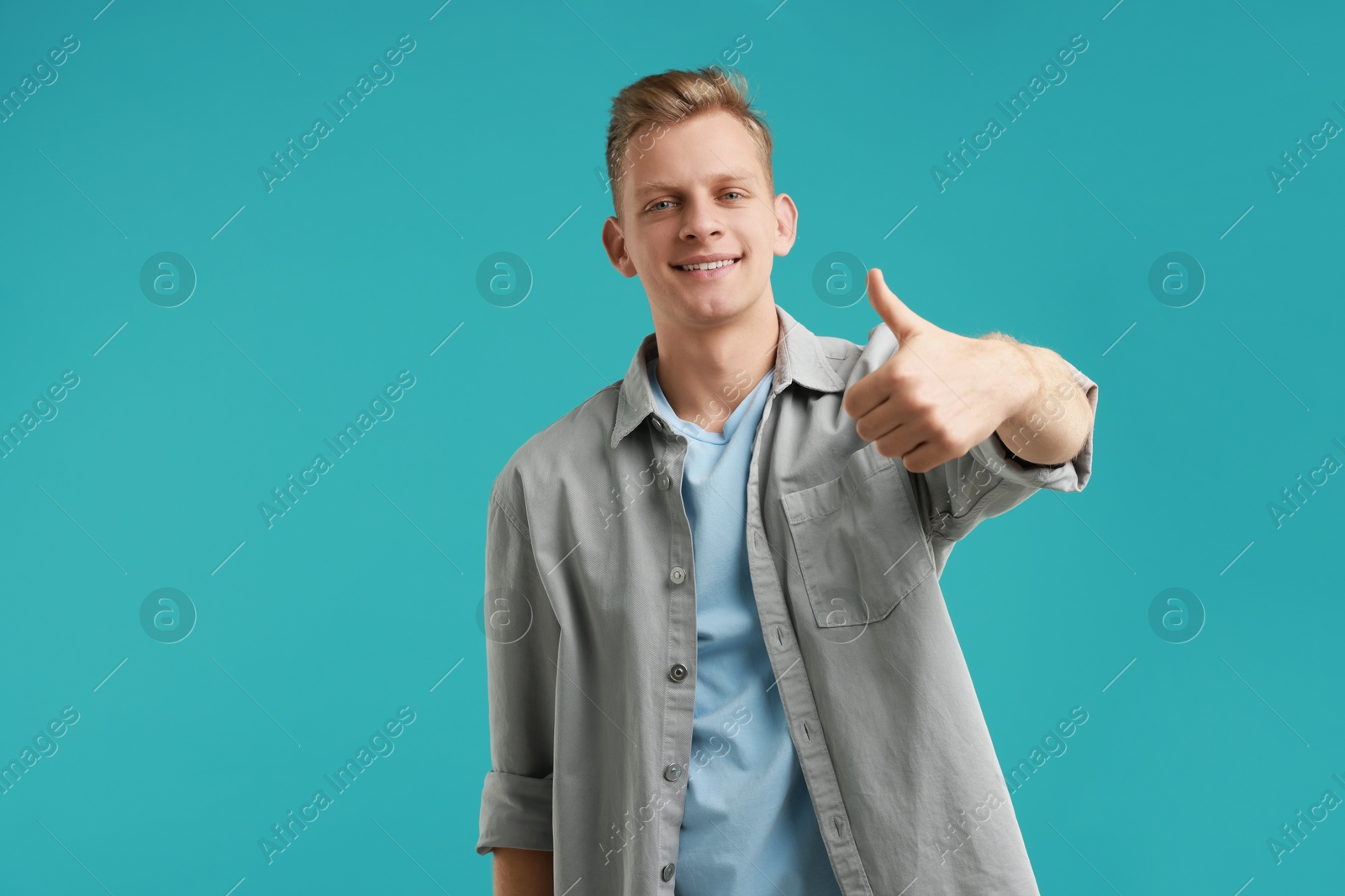 Photo of Happy man showing thumbs up on light blue background. Like gesture