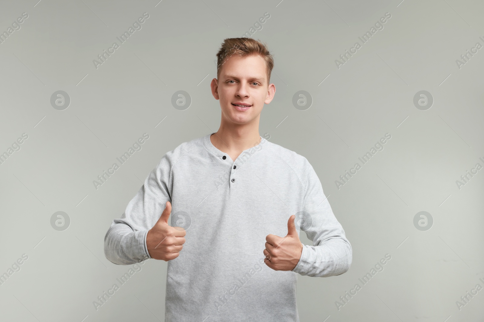 Photo of Happy man showing thumbs up on grey background. Like gesture