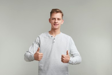 Photo of Happy man showing thumbs up on grey background. Like gesture