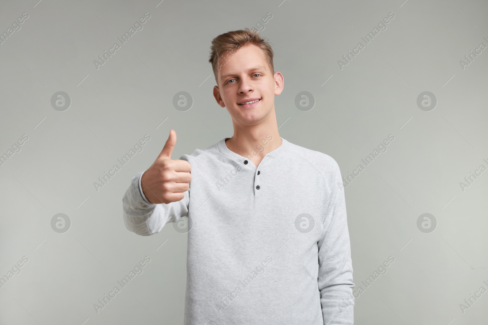 Photo of Happy man showing thumbs up on grey background. Like gesture