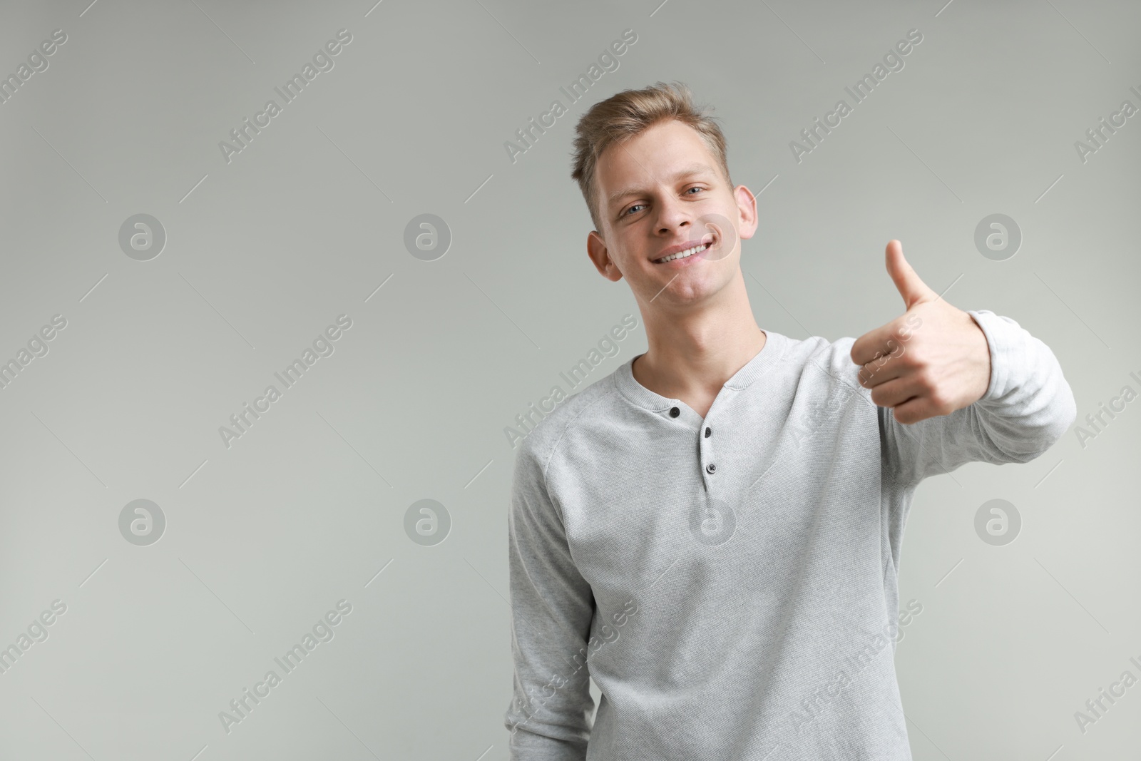 Photo of Happy man showing thumbs up on grey background, space for text. Like gesture