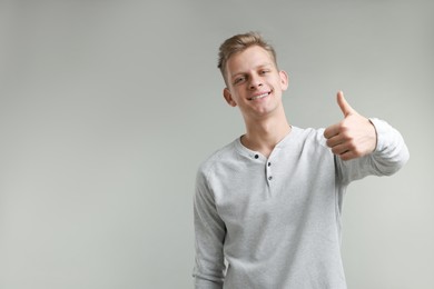 Happy man showing thumbs up on grey background, space for text. Like gesture