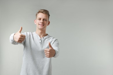 Photo of Happy man showing thumbs up on grey background, space for text. Like gesture