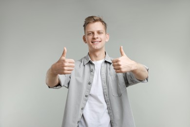 Happy man showing thumbs up on grey background. Like gesture