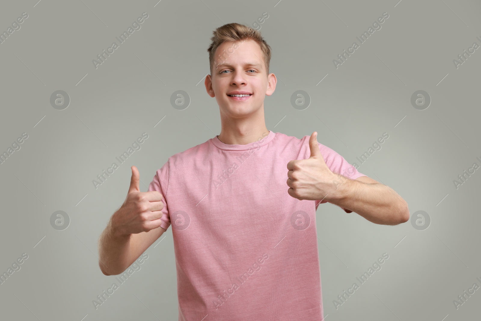 Photo of Happy man showing thumbs up on grey background. Like gesture