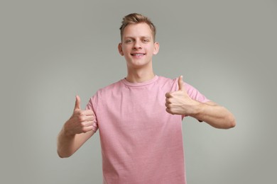 Photo of Happy man showing thumbs up on grey background. Like gesture