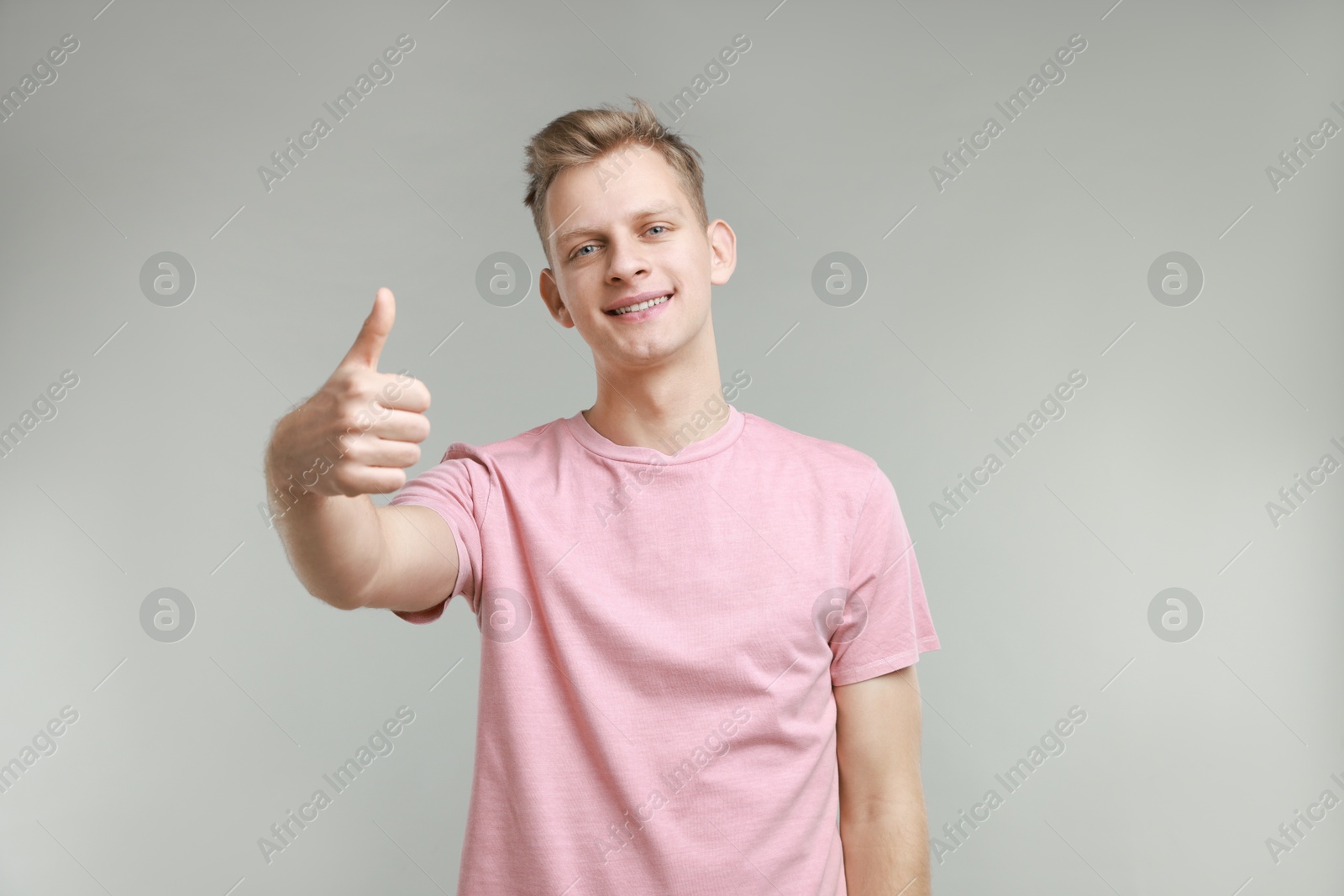 Photo of Happy man showing thumbs up on grey background. Like gesture