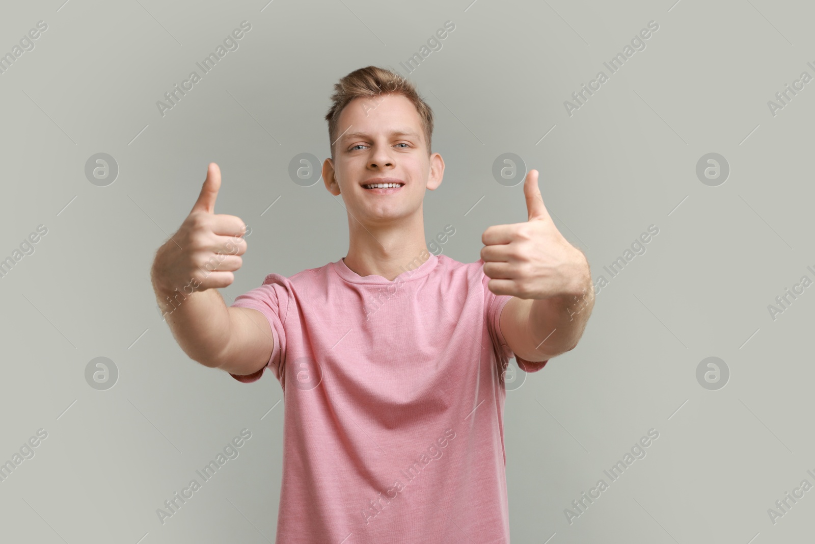 Photo of Happy man showing thumbs up on grey background. Like gesture