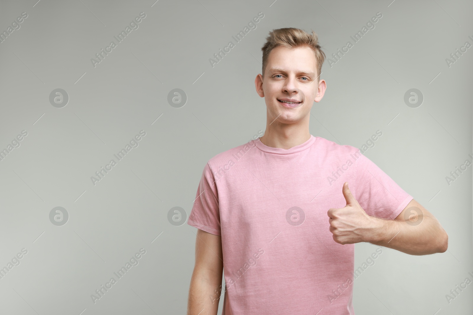 Photo of Happy man showing thumbs up on grey background, space for text. Like gesture