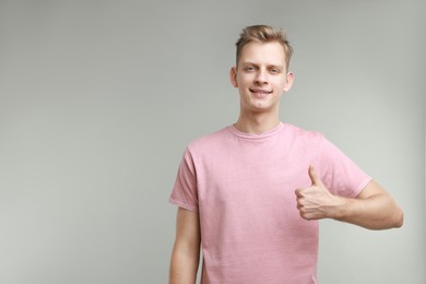 Happy man showing thumbs up on grey background, space for text. Like gesture