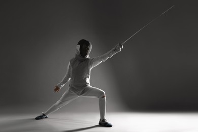 Photo of Fencer with epee practicing on gray background