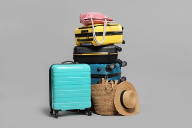 Photo of Stack of colorful suitcases, beach bags and straw hat on grey background