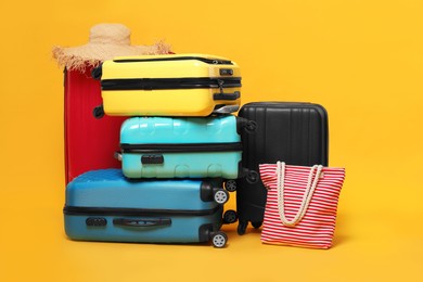 Photo of Many colorful suitcases, beach bag and straw hat on orange background