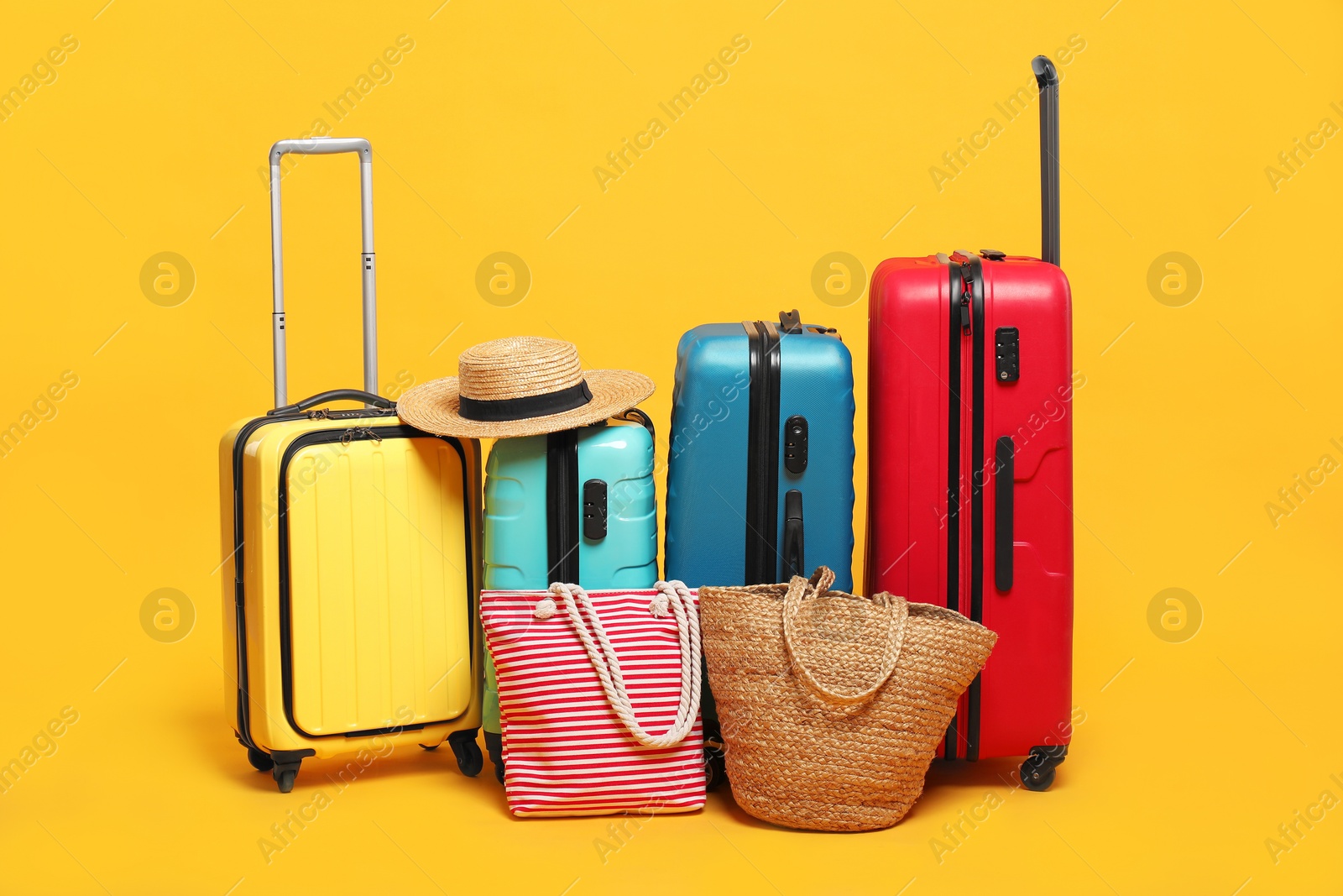 Photo of Many colorful suitcases, beach bags and straw hat on orange background