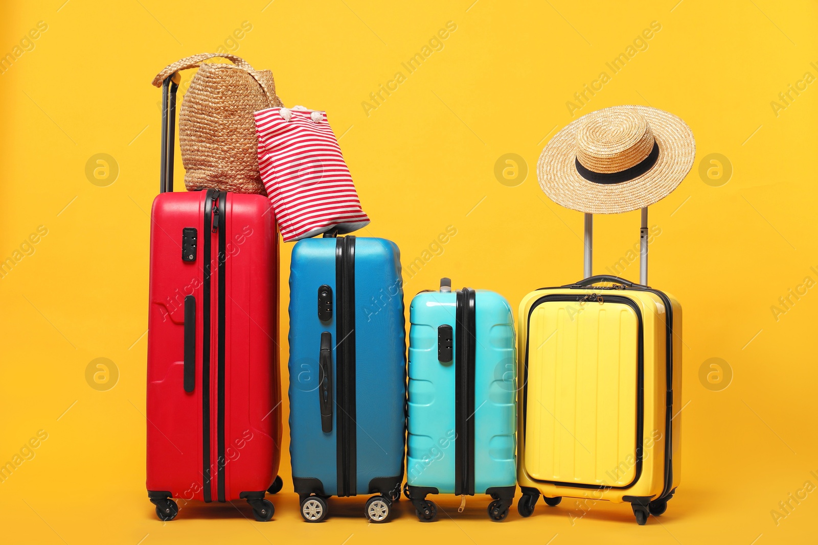 Photo of Many colorful suitcases, beach bags and straw hat on orange background