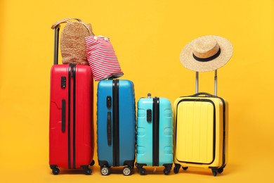 Photo of Many colorful suitcases, beach bags and straw hat on orange background