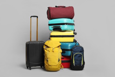 Photo of Stack of colorful suitcases, backpacks and bag on grey background