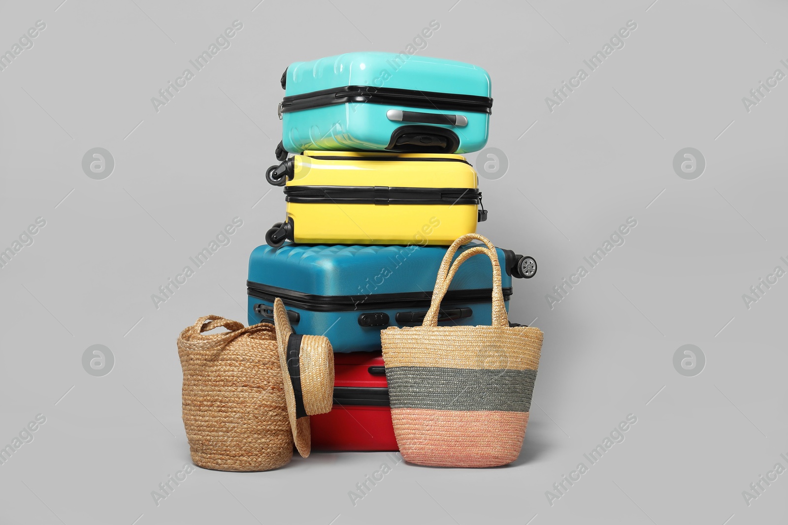 Photo of Stack of colorful suitcases, beach bags and straw hat on grey background