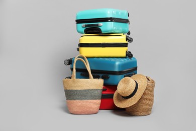 Photo of Stack of colorful suitcases, beach bags and straw hat on grey background