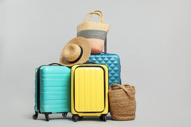 Photo of Many colorful suitcases, beach bags and straw hat on grey background