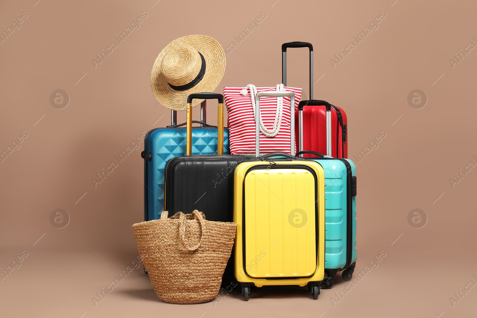 Photo of Many colorful suitcases, beach bags and straw hat on beige background