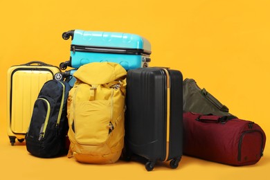 Photo of Pile of colorful suitcases, bags and backpacks on orange background