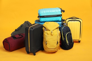 Photo of Pile of colorful suitcases, bags and backpacks on orange background