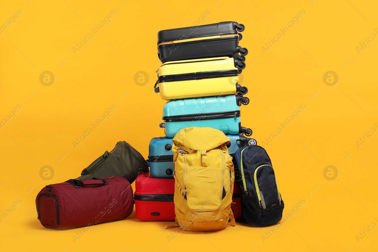 Photo of Stack of colorful suitcases, bags and backpacks on orange background