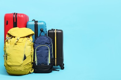 Photo of Colorful suitcases and backpacks on light blue background. Space for text