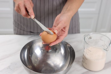 Photo of Making dough. Woman adding egg into bowl at white marble table, closeup