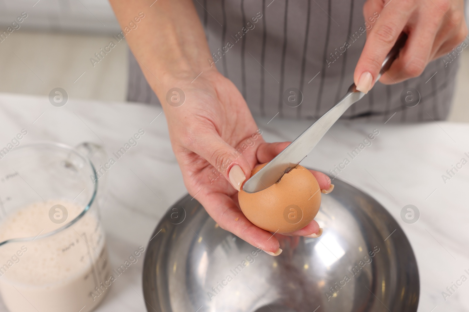 Photo of Making dough. Woman adding egg into bowl at white marble table, closeup