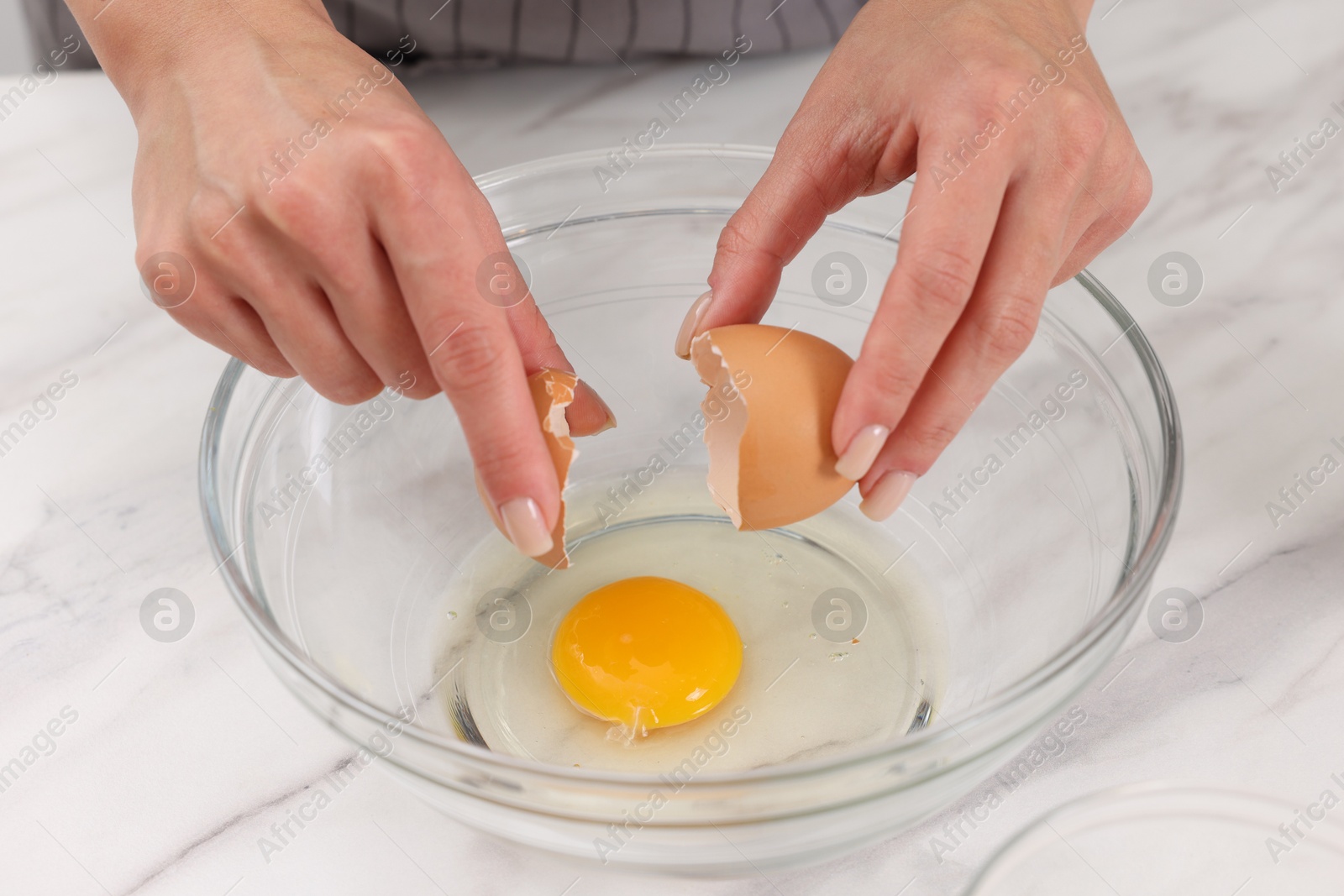 Photo of Making dough. Woman adding egg into bowl at white marble table, closeup