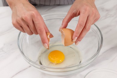 Making dough. Woman adding egg into bowl at white marble table, closeup